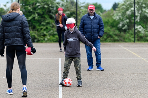 A boy wearing a blindfold tries blind football in a playground