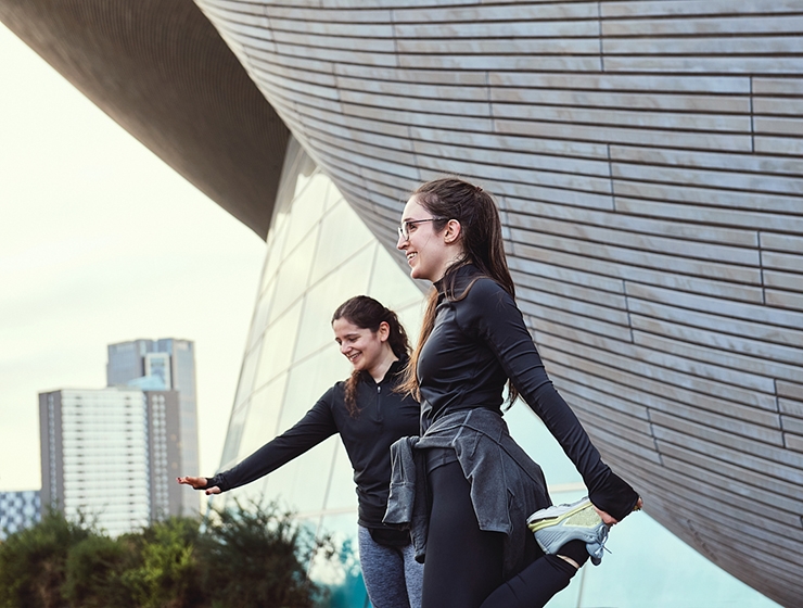 Two young women stretch before going for an outdoor run.